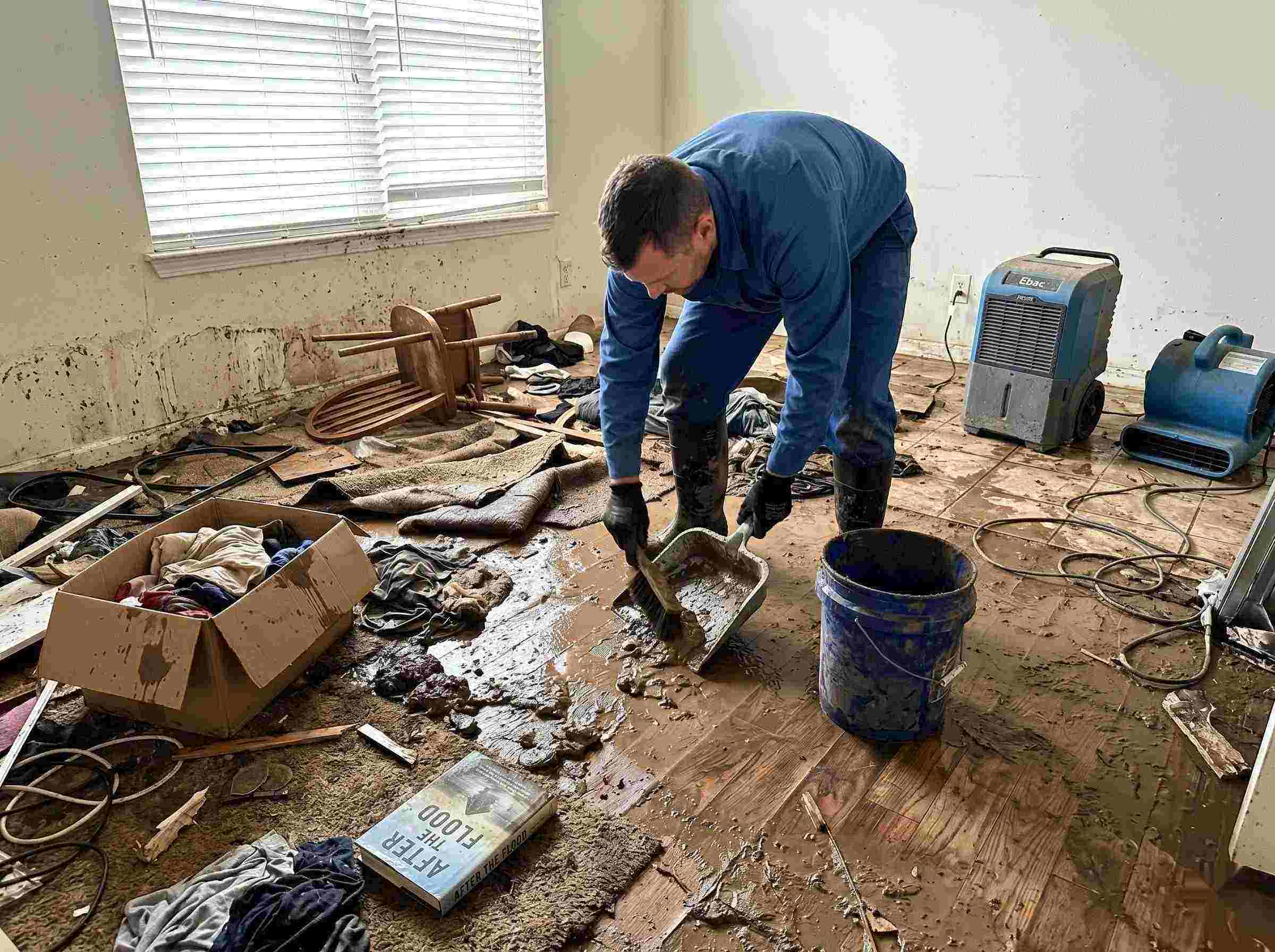 Realistic photo of a technician performing mud and debris removal after a home flood in St. Petersburg, showing soaked furniture, wet flooring, and scattered debris during post-flood cleanup.